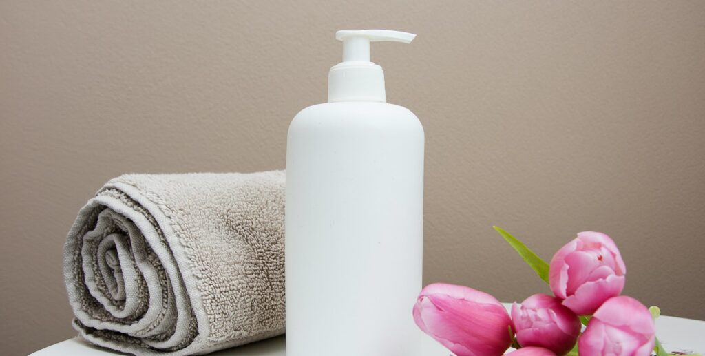 white plastic pump bottle beside pink tulips and gray towel