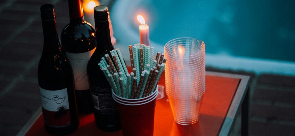 three wine bottles near cup and candle on square red table