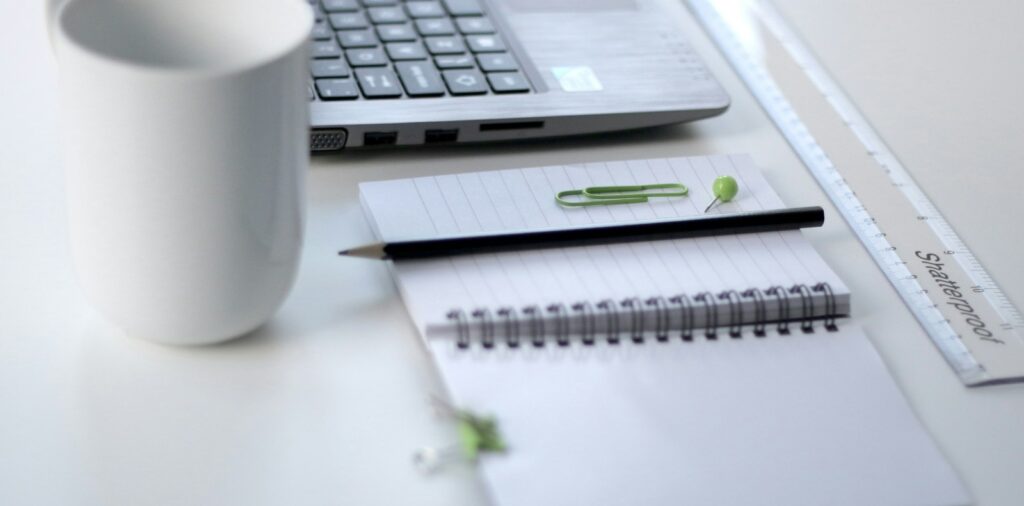 black pencil on ruled notepad beside white ceramic mug and gray laptop computer